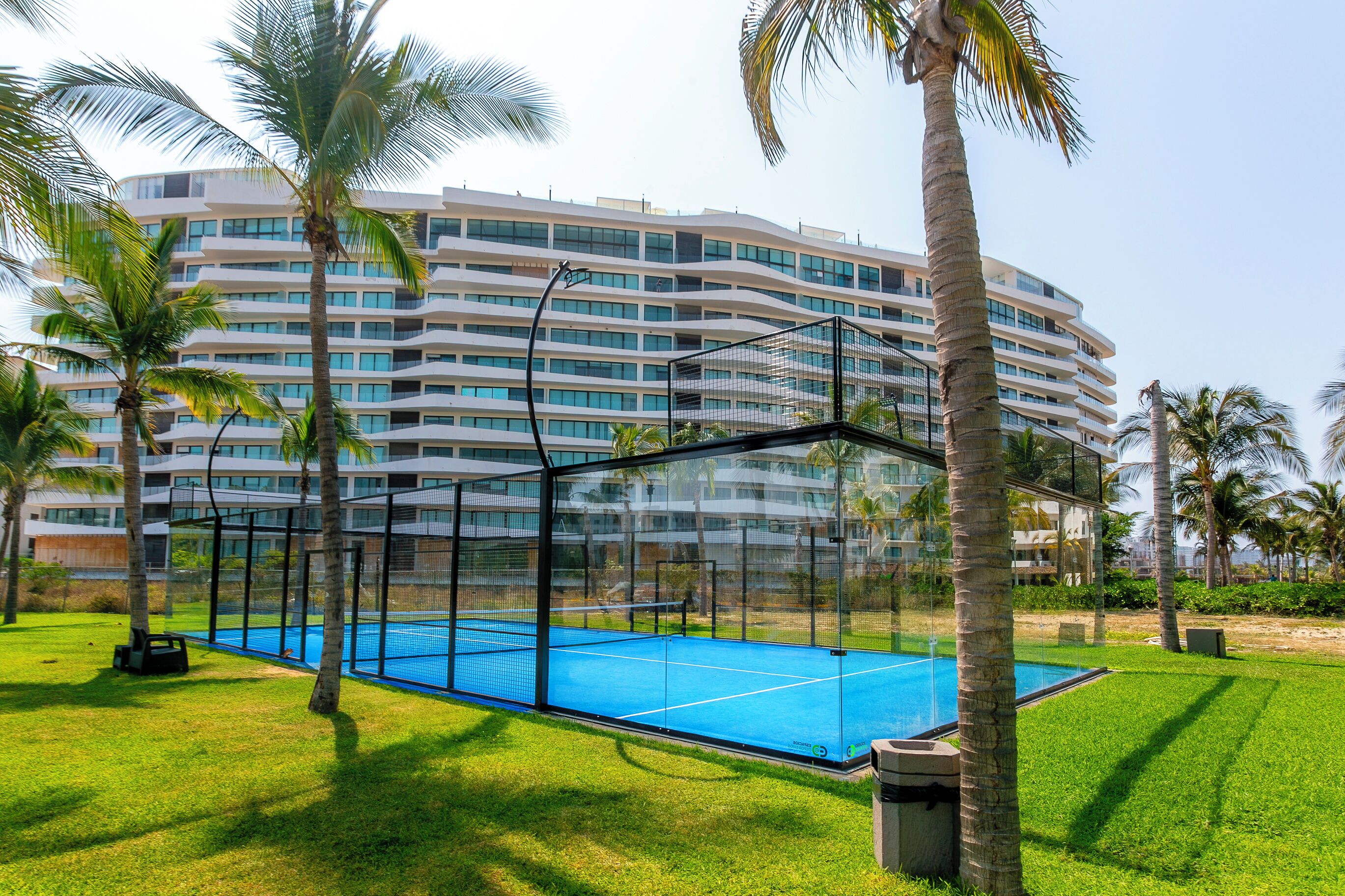 A hotel with a large, multi-story building, a tennis court, and palm trees.