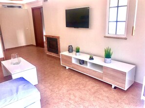 Ein Wohnzimmer mit Flachbildfernseher, einem weißen Konsolentisch mit Pflanzen, einem Kamin und einem gefliesten Boden.