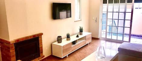 A living room with a fireplace, a TV mounted on the wall, a white console table, and a sliding glass door leading to an outdoor area.