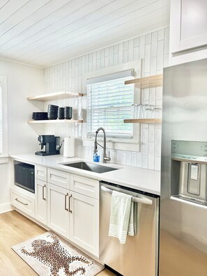 A modern kitchen with white cabinetry, a built-in dishwasher, a stainless steel refrigerator, and a window with blinds. - The Mullaney-Close to the Expo Center, Churchill Downs, and L&N Football Stadium (Louisville)