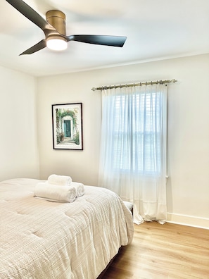 A bedroom with a bed, a ceiling fan, a window with sheer curtains, and a framed picture on the wall. - The Mullaney Near Expo Center (Louisville)