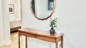 A wooden console table with a mirror, a vase with a plant, and a bed in the background. - Louisville Home by Kentucky Exposition Center & Churchill Downs (Louisville)