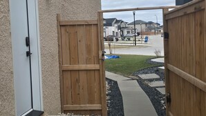 Een woning met een houten poort, een betonnen trap naar een deur en een welkomstmat.