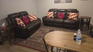 Een woonkamer met een donker leren bank, een houten salontafel, een vloerkleed met een patroon en een schilderij aan de muur.