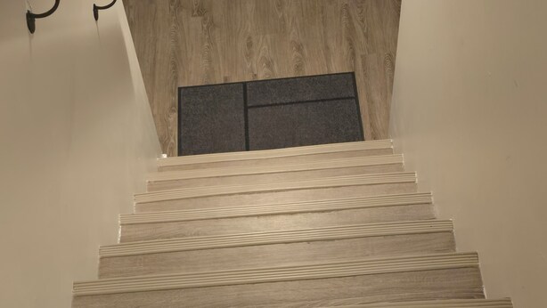 Een houten trap met een modern ontwerp, die uitkomt op een donker gebied.
