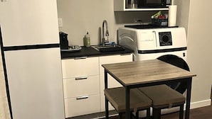 Eine kompakte Küche mit Kühlschrank, Mikrowelle, Wasserkocher und einem kleinen Tisch mit zwei Stühlen.