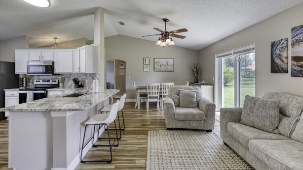 A spacious kitchen with white cabinets, a marble countertop, and a dining area with a white table and chairs. - Last Mango in Palm Coast (Palm Coast)