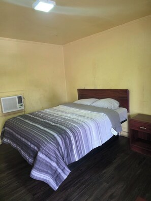 Una cama individual con cabecera de madera, una mesita de noche y un aire acondicionado instalado en la pared.