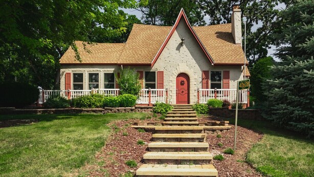 A two-story house with a red door and white trim, a front porch with a white railing, and a driveway leading to the front door. - Whimsical Historic Getaway Near Golf, Skiing and Wisconsin Southern Lakes (Genoa City)