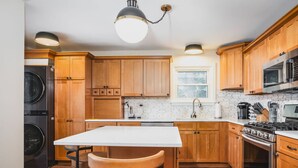 A modern kitchen with wooden cabinets, a central island, a built-in stove, and a washing machine. - Whimsical Historic Getaway Near Golf, Skiing and Wisconsin Southern Lakes (Genoa City)