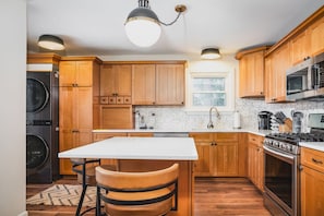 A kitchen with wooden cabinets, a stainless steel stove, a microwave, and a washing machine.