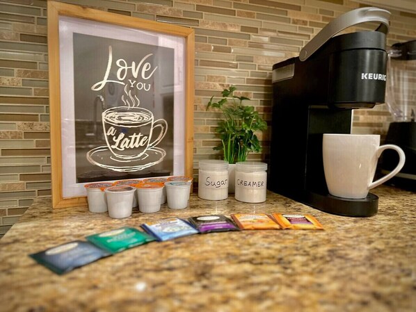 A coffee maker, sugar and creamer containers, and coffee pods on a kitchen counter. - Kingbed W/pool/gym/bbq@theheights,longstaydiscount (Houston)