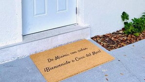 En hvid dør med dørmåtte, der står 'De Miami, con sabor Bienvenido a Casa del Mar!'.