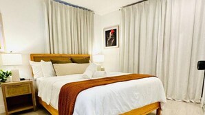 Et hotelværelse med seng, natbord, lampe og gardiner.