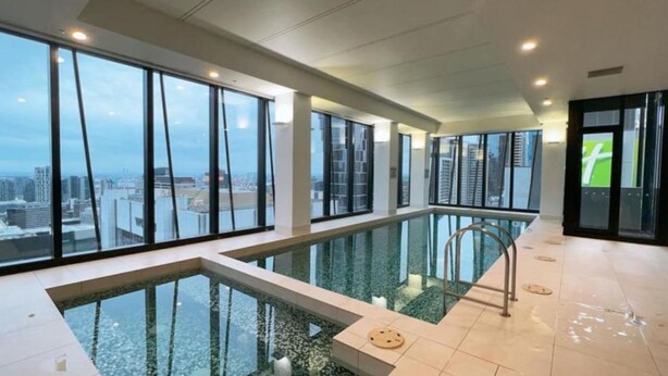 Une piscine intérieure moderne dotée de grandes baies vitrées offrant une vue sur la ville.