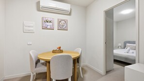 Une petite pièce propre, avec une table de salle à manger ronde, deux chaises, un lit et un climatiseur.