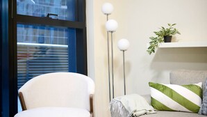 Une pièce comprenant une chaise, un lampadaire, une plante et un canapé avec des coussins.