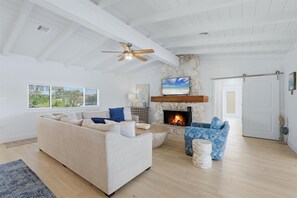 A living room with a stone fireplace, a ceiling fan, and a large window with blinds. - Beautiful GROUND LEVEL Pool home, totally renovated ...PET FRIENDLY! (Placida)