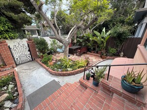 Eine Ziegelterrasse mit Garten, ein Metallzaun und eine Treppe, die zu einem Haus führt.