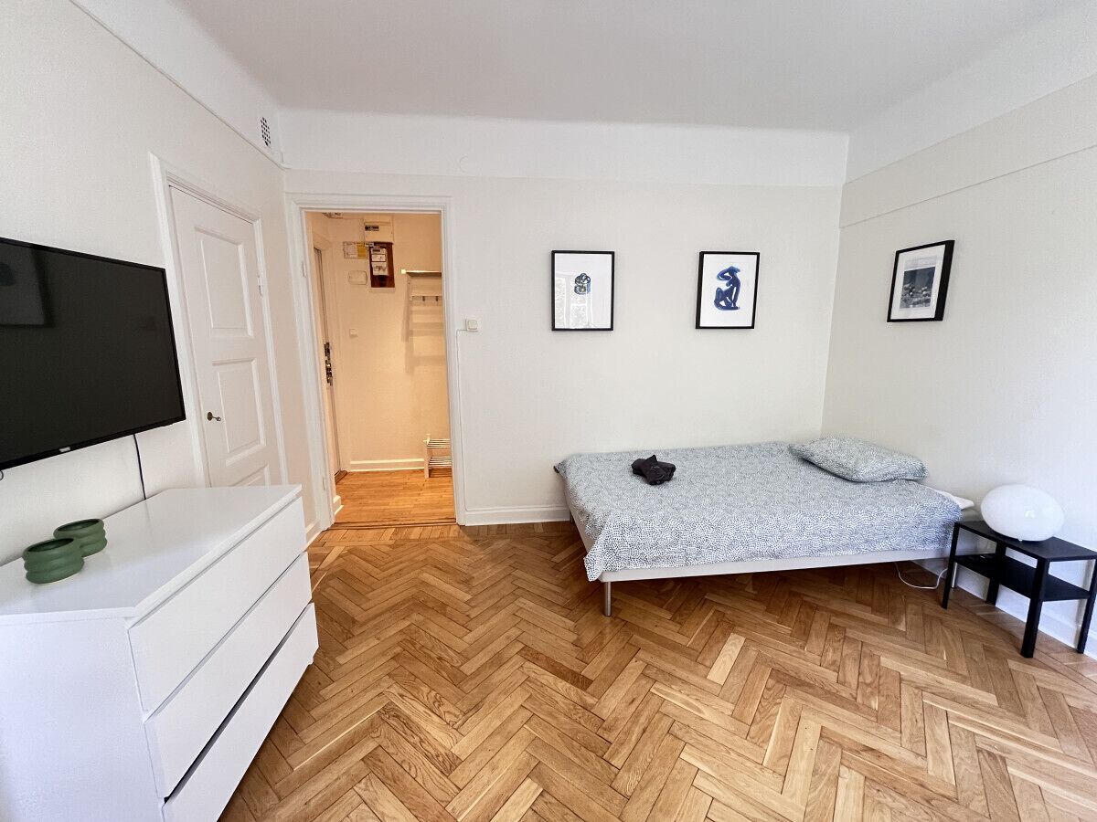 Ein Schlafzimmer mit einem Bett, einem Fernseher, einem Schminktisch und einer Tür zu einem anderen Raum.
