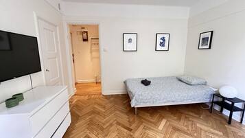 Ein Schlafzimmer mit einem Bett, einem Fernseher, einem Schminktisch und einer Tür zu einem anderen Raum.