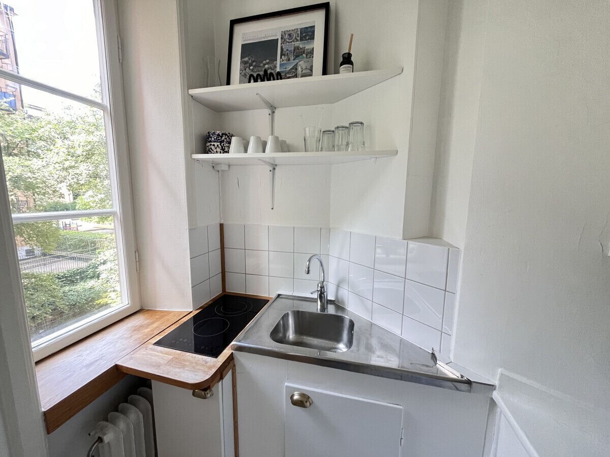 A compact kitchen with a window, white tiles, a sink, and a small countertop.