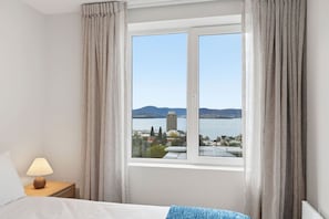 A hotel room with a bed, a nightstand with a lamp, and a window with curtains. - Designer Stay w/ River Views (Sandy Bay)