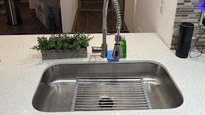 Een moderne keuken met een roestvrijstalen spoelbak, een hangende hanglamp en een klein plantje op het aanrecht.
