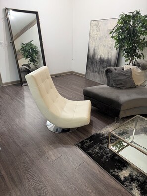 A modern living room with a cream-colored chair, a dark sofa, a glass coffee table, and a large abstract painting. -     Peaceful Chamblee Escape Close to Buckhead & Downtown (Chamblee)