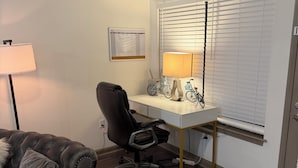 Een kamer met een bureau, stoel, lamp en een bank.