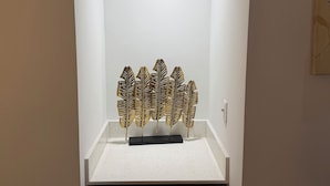 Een kamer met een wit plafond, een lamp, kunstwerk aan de muur en een zwart object op een witte ondergrond.