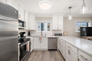 A modern kitchen with white cabinets, stainless steel appliances, a dishwasher, a coffee maker, and a toaster. - Midtown OC Retreat | Ocean Block | Sleeps 10 (Ocean City)