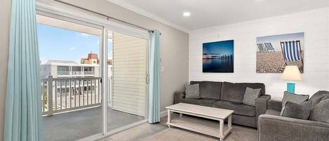 A living room with a sofa, a coffee table, and a balcony with curtains.