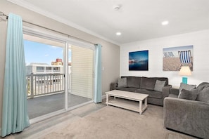 A living room with a sofa, a coffee table, and a balcony with curtains. - Midtown OC Retreat | Ocean Block | Sleeps 10 (Ocean City)