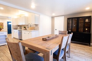 Ein Essbereich mit Holztisch und Stühlen, im Hintergrund eine Küche und ein schwarzes Schrank mit Glastüren.