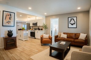 Ein modernes Wohnzimmer mit einem braunen Ledersofa, einem Couchtisch und einer Küche im Hintergrund.