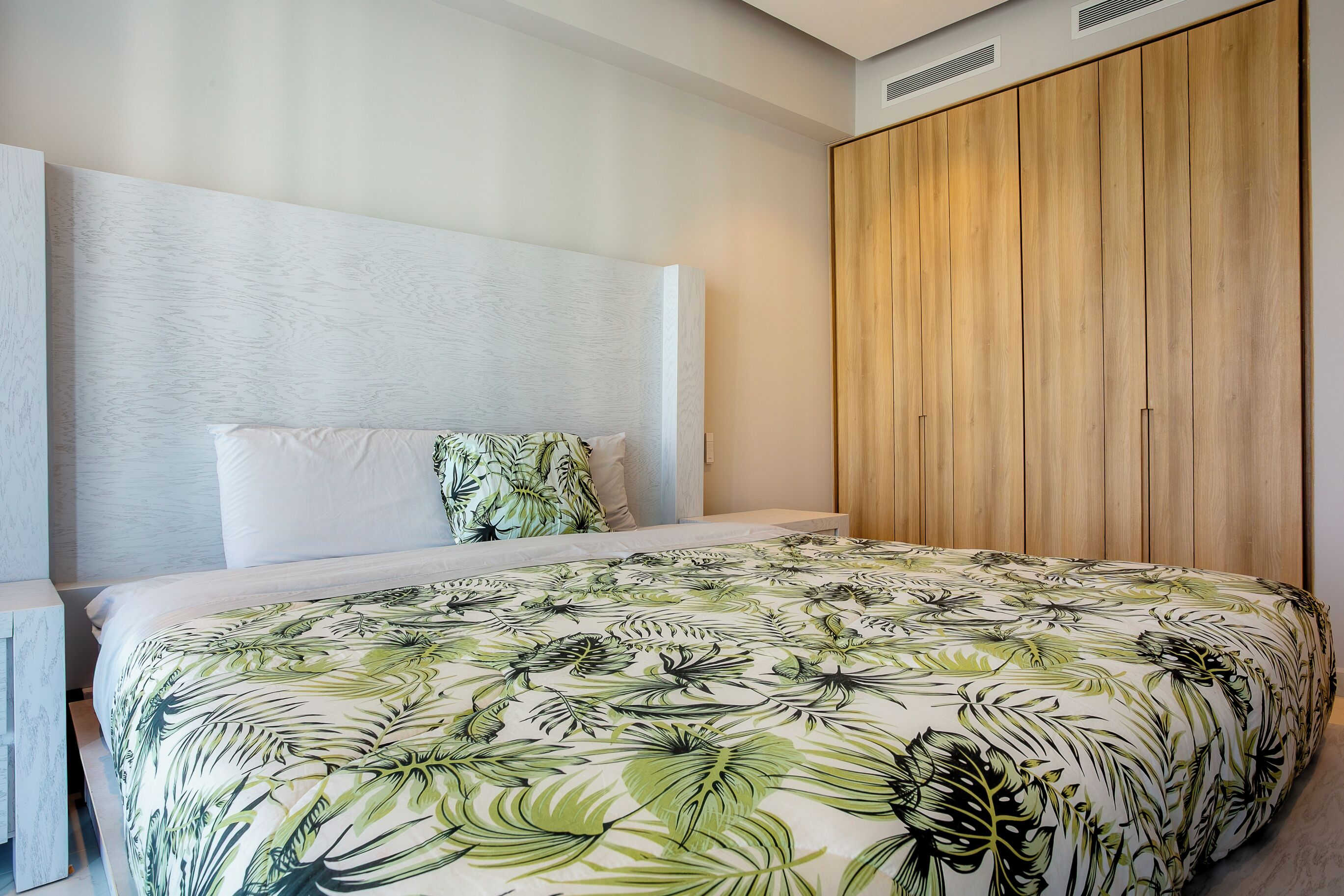 A bedroom with a large bed, a wooden wardrobe, and a white headboard.