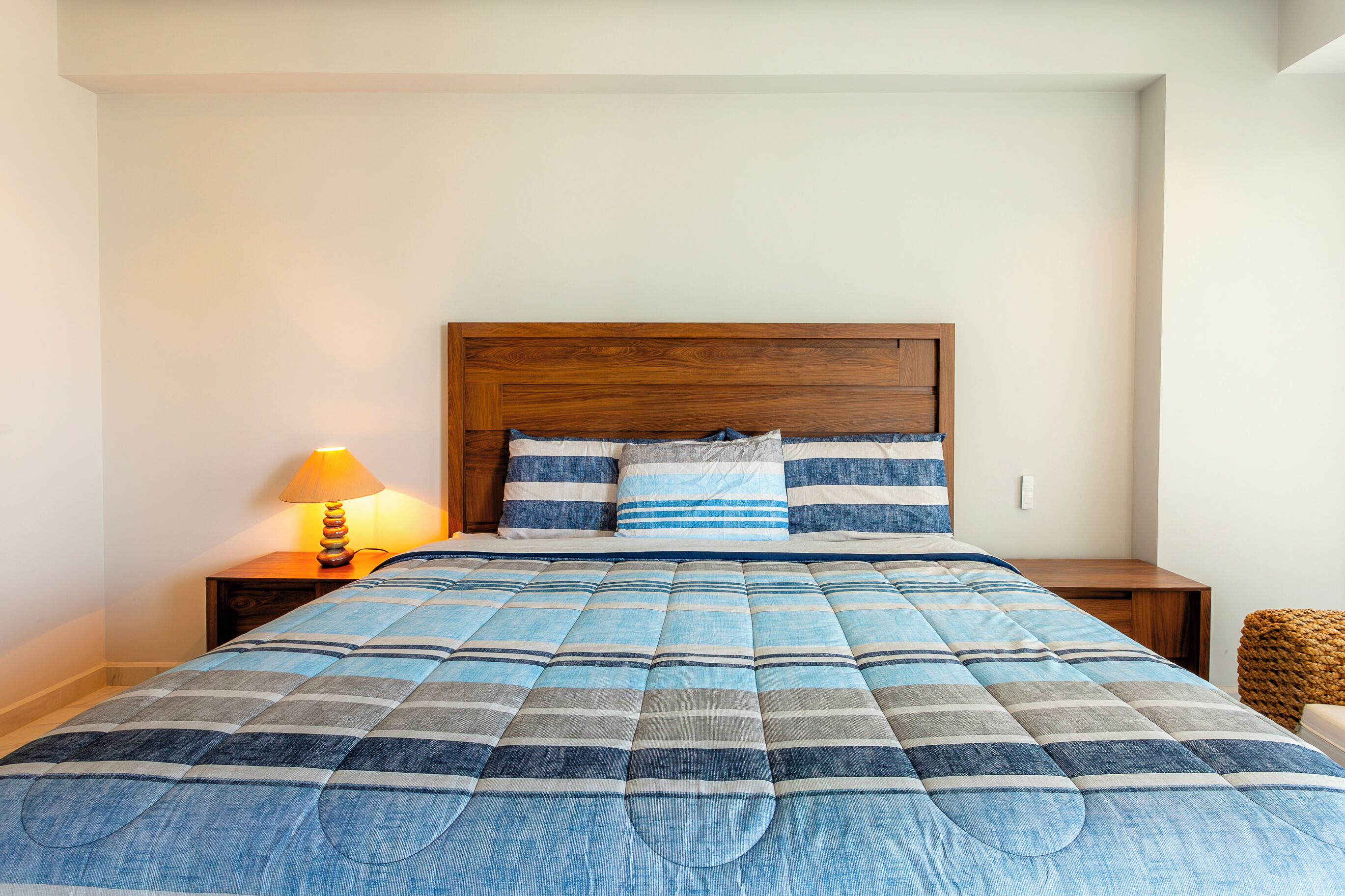 A bed with a blue and gray striped comforter, a wooden headboard, and a bedside lamp.