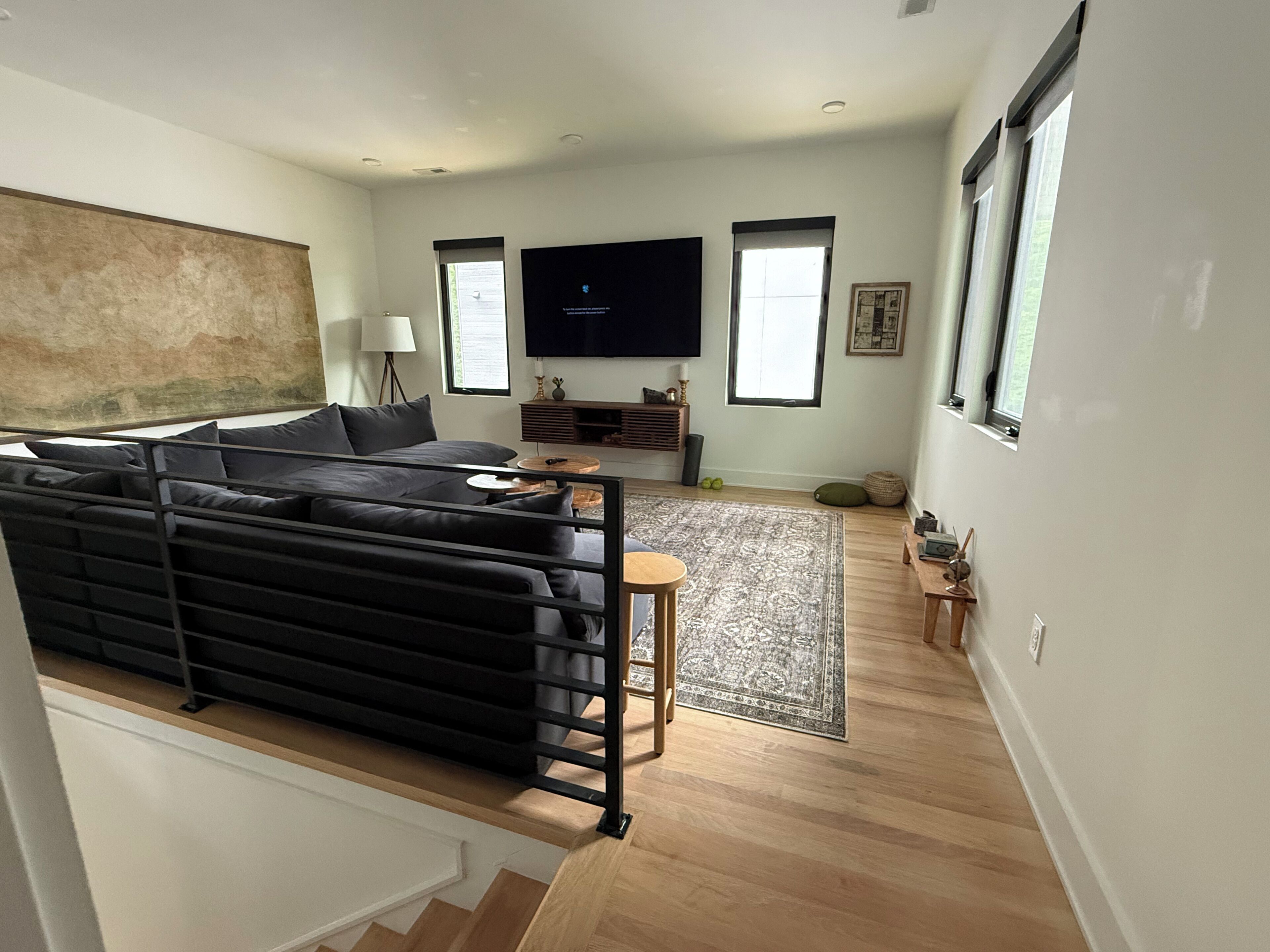 A modern living room with a black sofa, a flat-screen TV, a wooden coffee table, and a patterned rug.