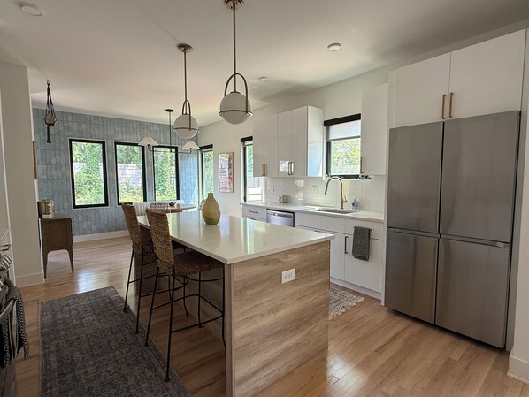 A modern kitchen with a central island, stainless steel appliances, and large windows.