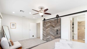 Une chambre à coucher moderne avec un lit, un ventilateur de plafond, un grand miroir et une porte de placard coulissante.