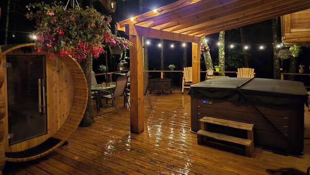 A wooden deck with a hot tub, seating area, and string lights.