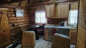 A log cabin interior with a dining area, kitchen, and two chairs.