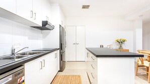 Una cocina moderna con armarios blancos, encimera negra, electrodomésticos de acero inoxidable y una zona de comedor de madera.