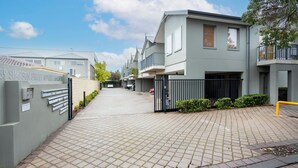 Un edificio residencial con entrada protegida por una reja, camino de entrada pavimentado y cielo despejado.