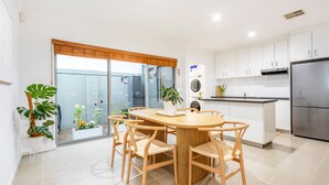Una cocina moderna con armarios blancos, un refrigerador de acero inoxidable y un comedor con mesa y sillas de madera.