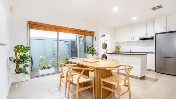 A modern kitchen with white cabinets, a stainless steel refrigerator, and a dining area with a wooden table and chairs.
