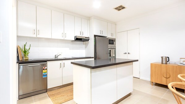 A modern kitchen with white cabinets, stainless steel appliances, a built-in oven, and a coffee machine.