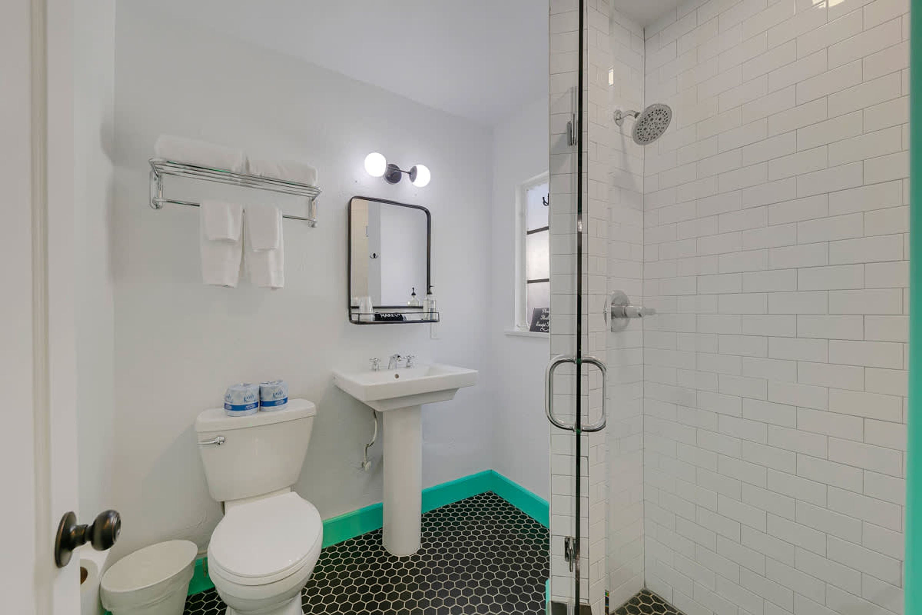 A bathroom with a toilet, sink, mirror, and shower.