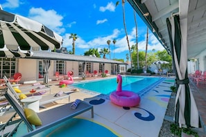 A pool area with lounge chairs, a pink flamingo float, and palm trees. - Spirit of Sofia 11bd (Palm Springs)